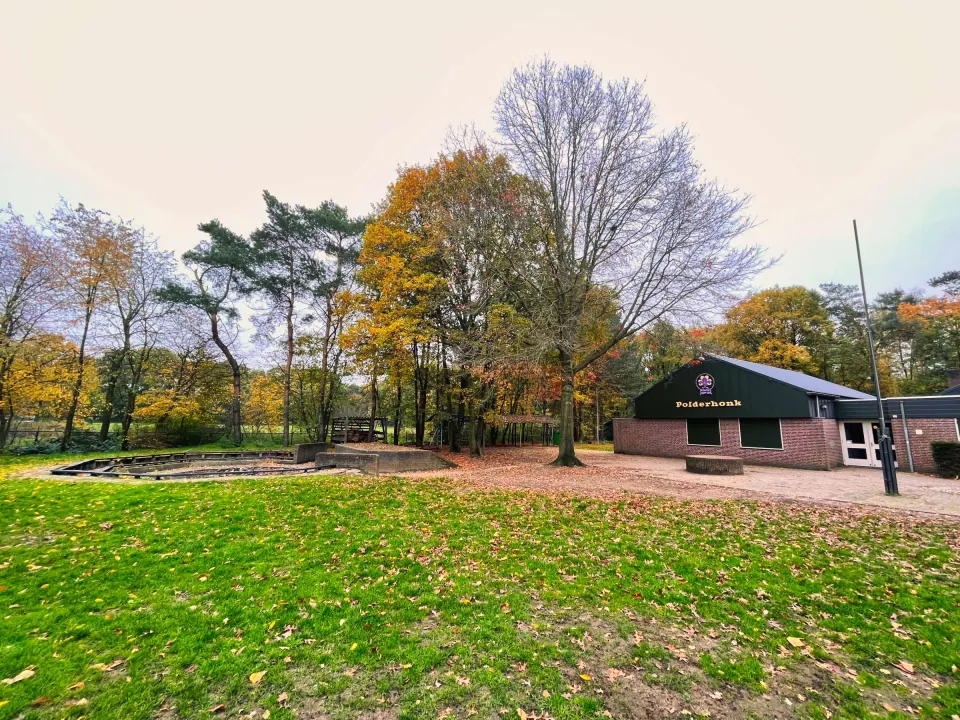 Een grasveld met een kampvuur plek (links) en de Blokhut van Scouting Asten (rechts)
